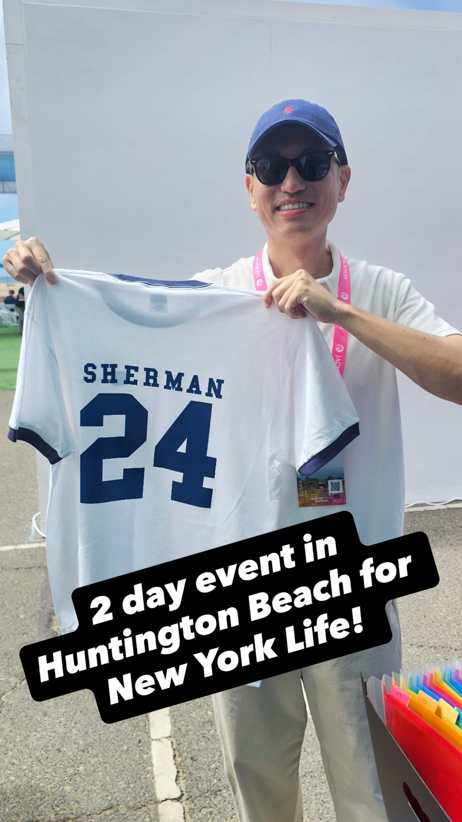 Smiling wedding guest holding up a personalized shirt with his name stitched-style across the back at a Huntington Beach event
