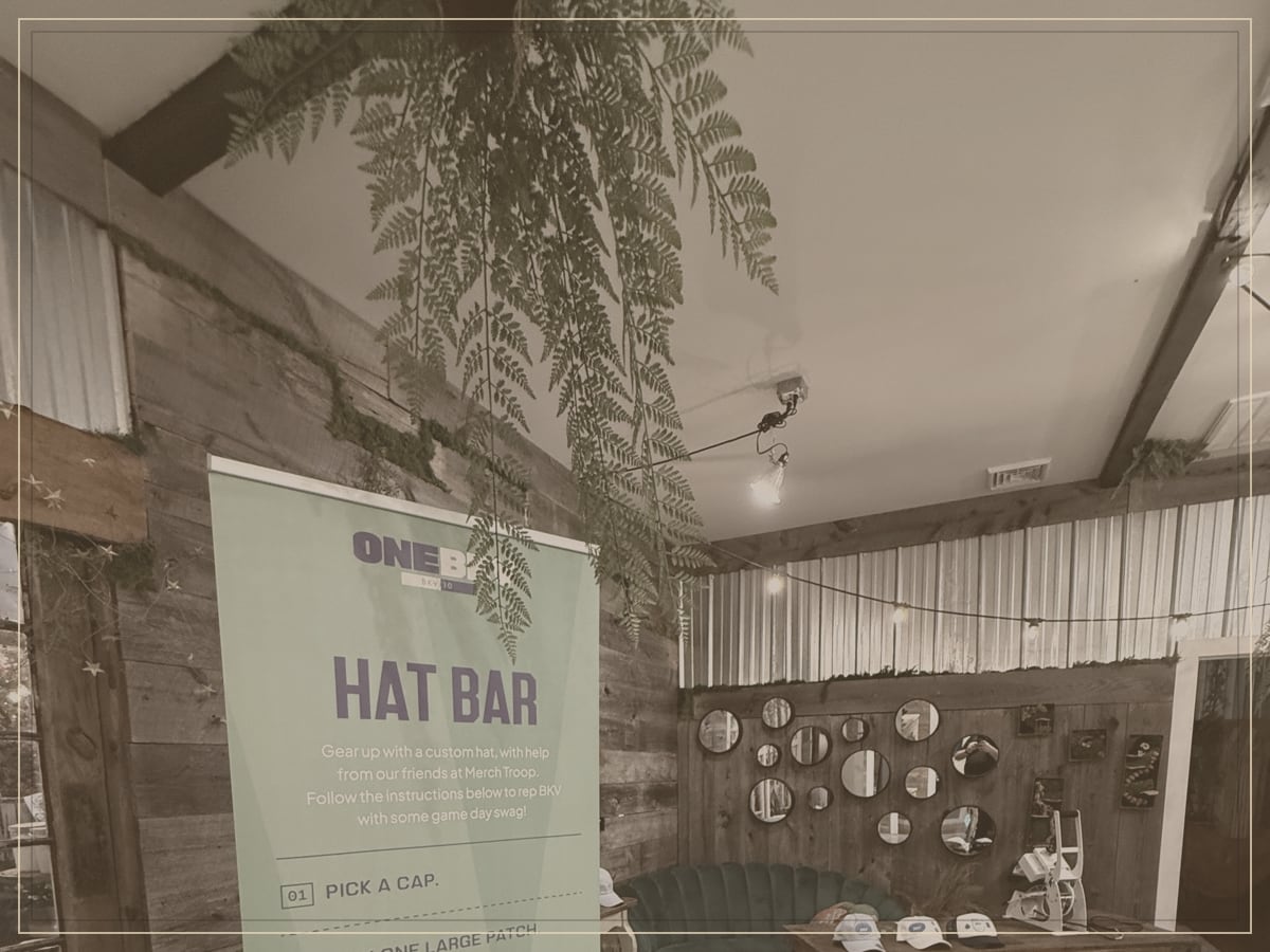 Sepia-toned view of a styled station vignette with greenery and a menu banner in a wood-paneled venue